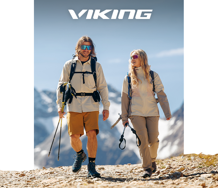 Two hikers in Viking outdoor gear walking with trekking poles and backpacks on a mountain trail, snowy peaks behind