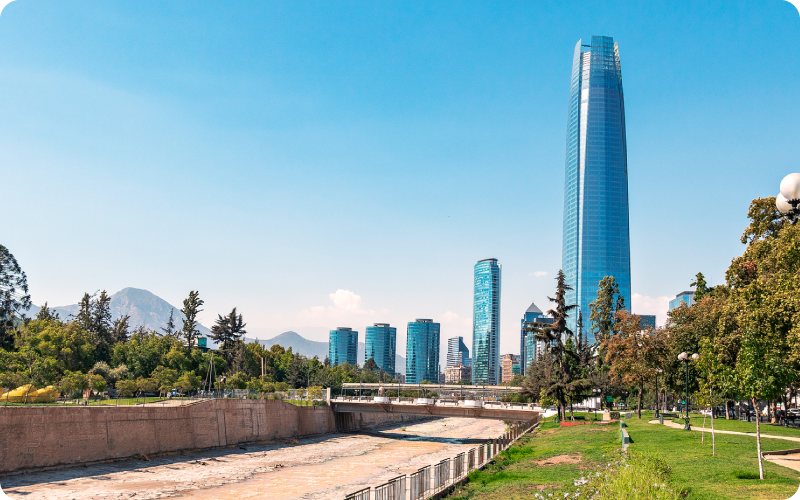 modern city skyline with a tall glass skyscraper, riverside park and dry riverbed under a clear blue sky