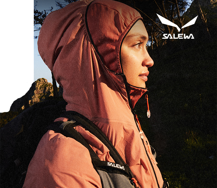 Profile of a person in a pink hooded jacket and backpack at sunset on a mountain trail, Salewa logo visible