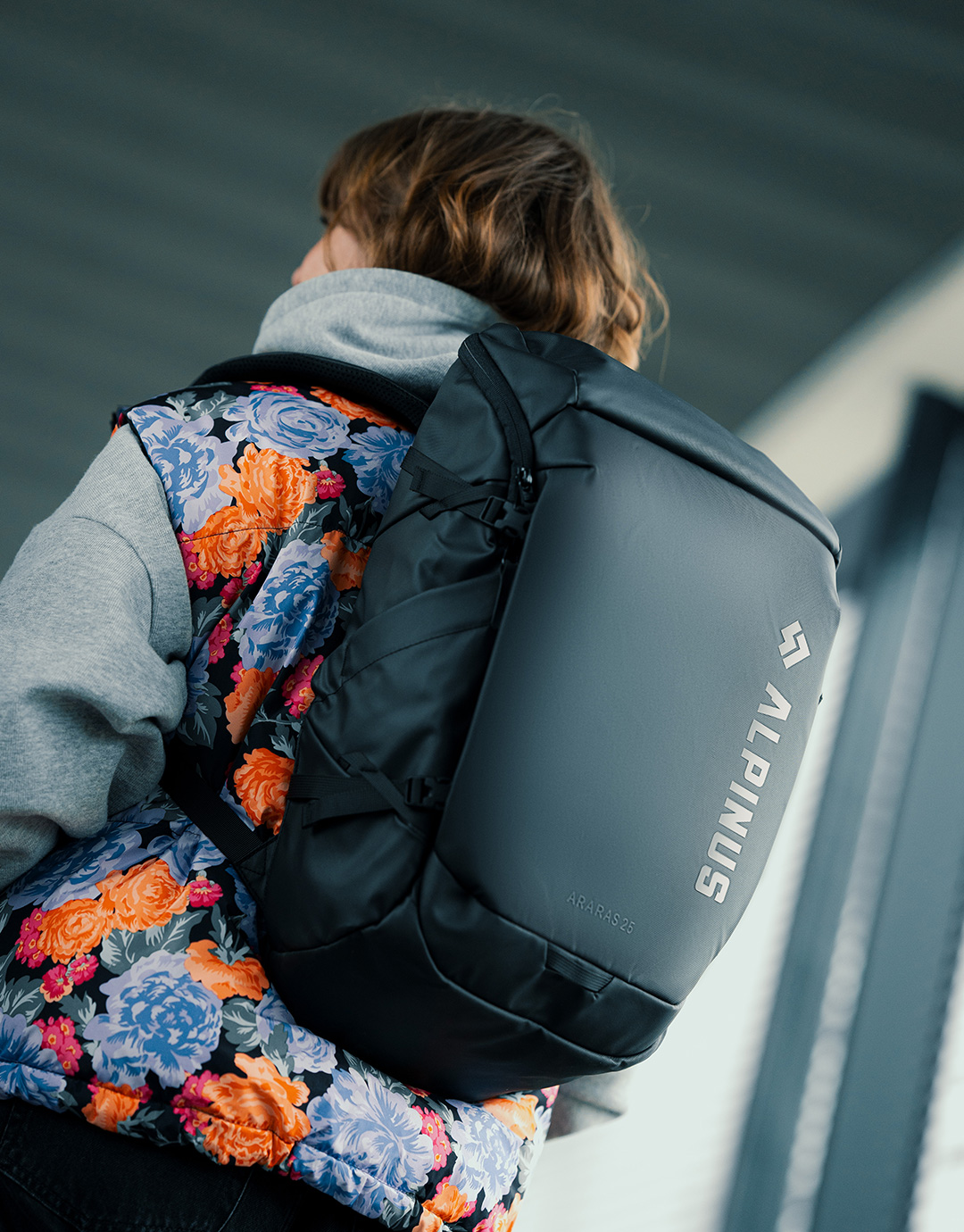 Rear view of person wearing a floral jacket and large black Alpinus backpack in an urban setting