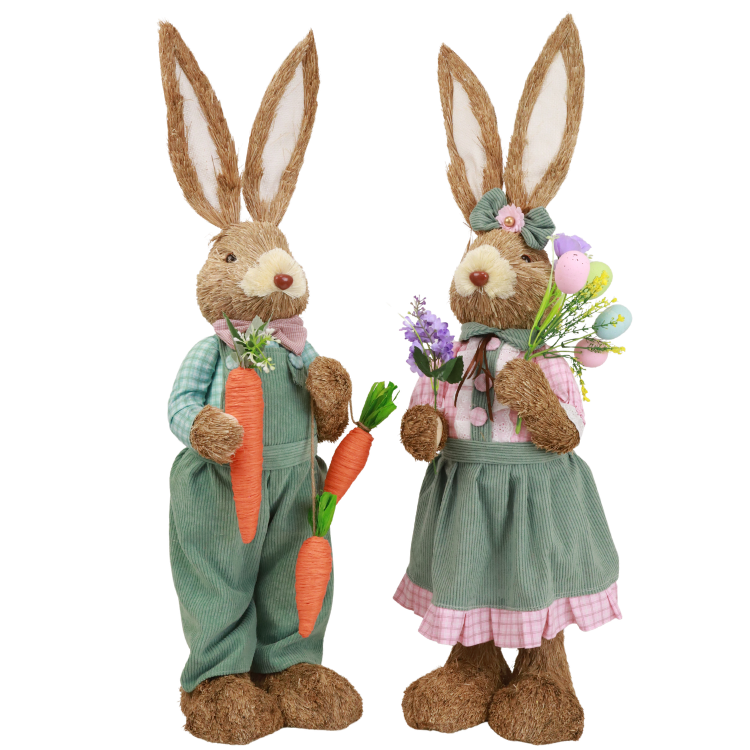 Two straw Easter bunnies on white background in green outfits, one holding carrots, the other a bouquet of flowers.