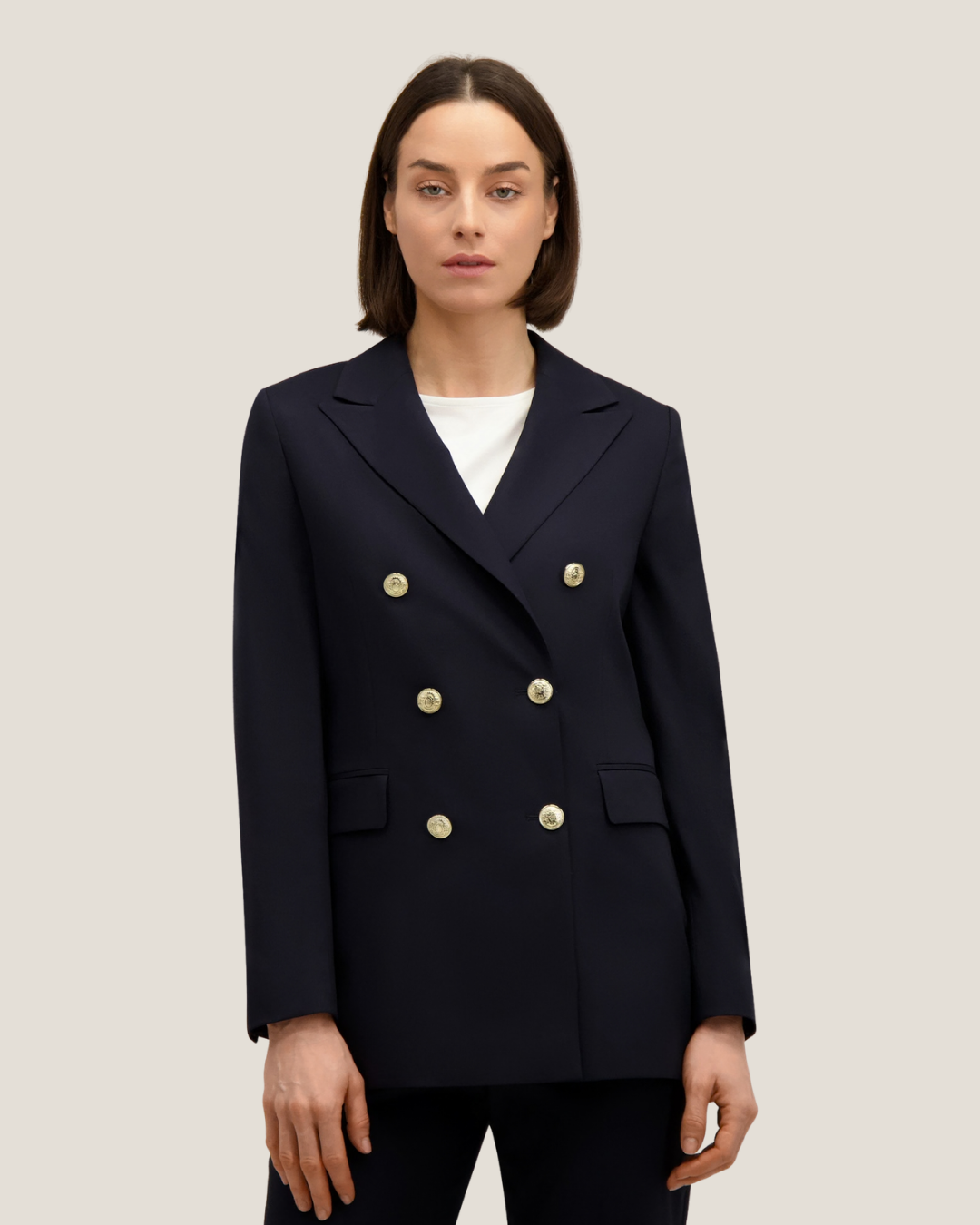 Model wearing navy double-breasted blazer with six gold buttons over a white top, standing against a neutral background