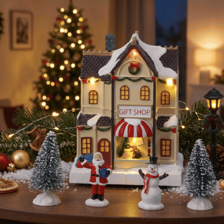 Festive miniature Christmas village display with illuminated gift shop, bookshop and theatre, decorated tree and tiny figurines