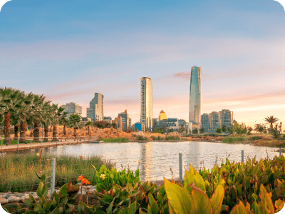 Sunset city skyline with modern skyscrapers, waterfront lake and palm-lined park in foreground