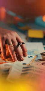 Hand wearing ring picking up a €50 banknote from scattered euro notes on a table