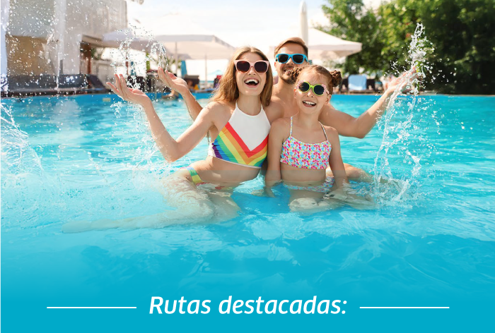Two adults and a child splashing in a resort pool on a sunny day, wearing sunglasses and colourful swimwear, smiling and enjoying holiday fun