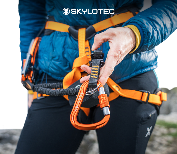 Close-up of climber adjusting orange Skylotec locking carabiner on an orange safety harness and lanyard
