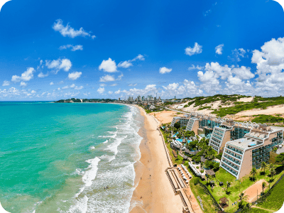 Turquoise ocean and sandy beach with beachfront hotels and distant city skyline under a bright blue sky