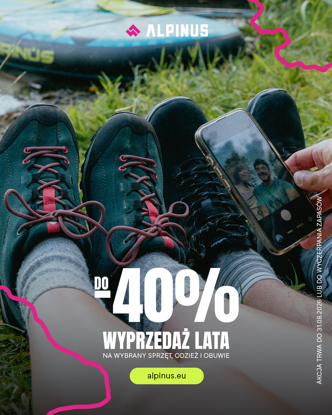 Two people wearing hiking shoes sitting on grass beside an inflatable kayak, one holding a phone showing their selfie — Alpinus promo