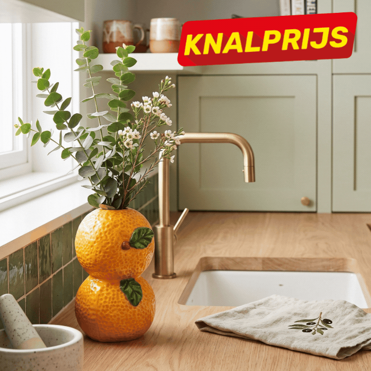 Modern green kitchen countertop with stacked oranges and watermelon vase, brass tap, linen cloth and potted foliage, 'Knalprijs' sale tag