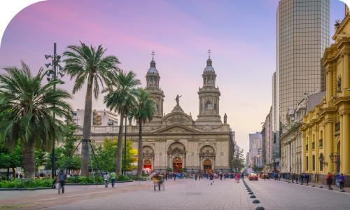 Metropolitan Cathedral in Santiago at sunset, palm‑lined plaza with pedestrians and historic buildings