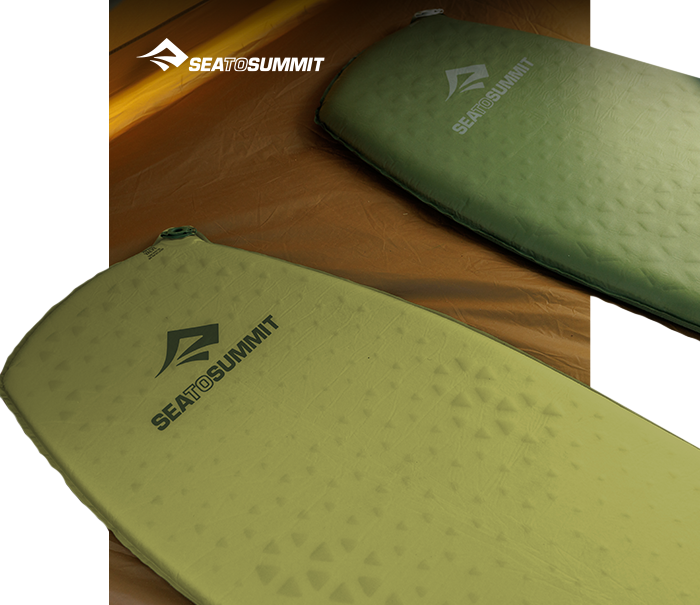 Two green Sea to Summit self-inflating sleeping mats with logo on a brown tent floor, angled view