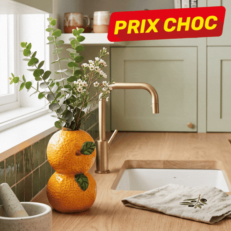 Ceramic fruit-shaped vases (stacked oranges and watermelon) holding flowers on a wooden kitchen sink counter with PRIX CHOC badge