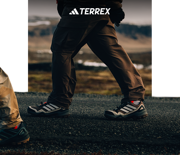 Close-up of a person walking on a gravel trail wearing adidas Terrex hiking shoes and waterproof trousers with moorland background