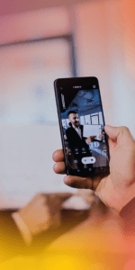 Hand holding smartphone filming a man in a suit during a video call or interview in a blurred office background