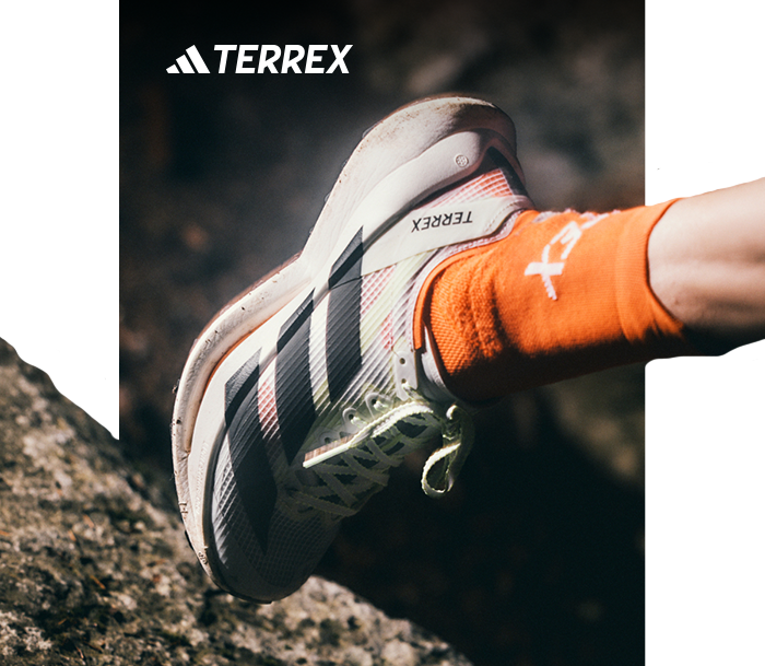 Close-up of an adidas TERREX trail running shoe on a climber's foot with bright orange socks, gripping rocky terrain