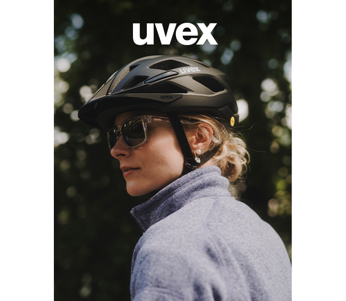 Profile of a woman wearing a black Uvex cycling helmet and sunglasses, grey fleece, blurred green background and UVEX logo