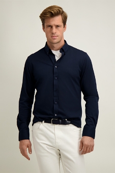 Man in navy button-down shirt and white trousers posing against a plain light background, men's smart-casual outfit