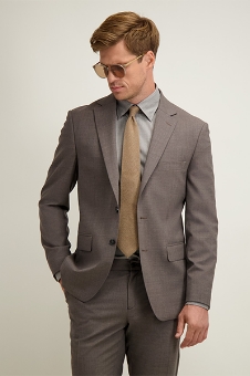 Man wearing tailored grey suit, light blue shirt, tan tie and sunglasses, posing with hands in pockets against a neutral background