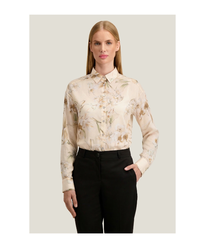 Woman wearing cream floral silk blouse tucked into black tailored trousers on neutral background