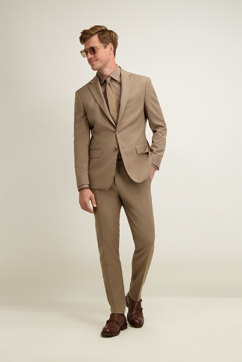 Man modelling tan tailored suit with matching tie, brown leather shoes and sunglasses, posing against plain studio backdrop