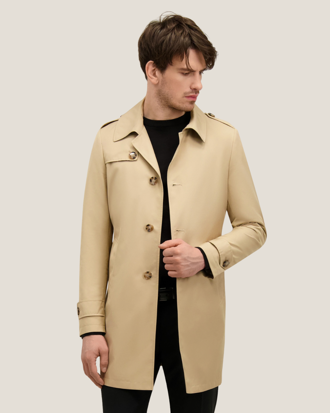 Man modelling beige single-breasted trench coat over black jumper, smart-casual style with front buttons and epaulettes