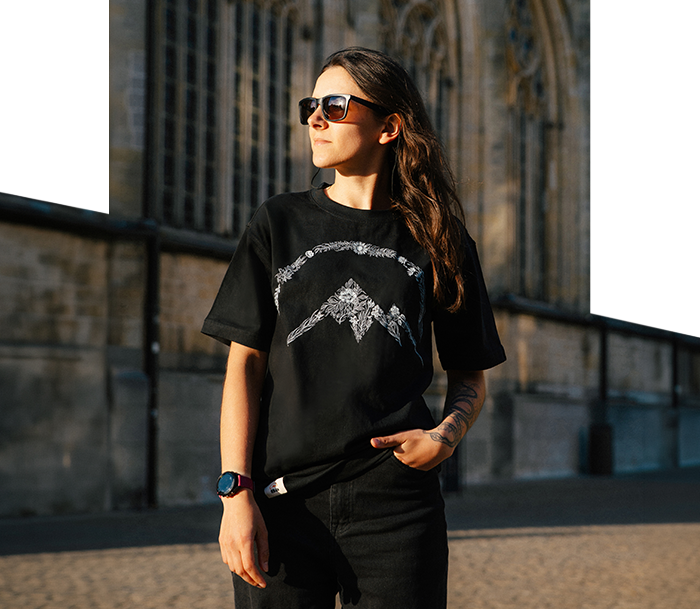 Person wearing sunglasses and black graphic T-shirt with tattoo and smartwatch, standing by a cathedral