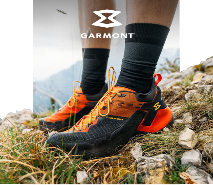 Garmont orange-and-black trail running shoes worn by hiker on rocky alpine terrain, close-up with visible logo