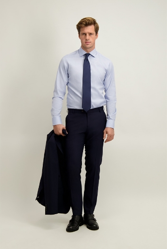 Man in business attire wearing a light blue shirt and navy tie, holding a navy suit jacket with navy trousers and black shoes