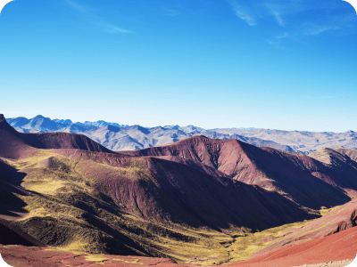 Panoramic view of colourful layered mountains and valleys under a clear blue sky, showcasing rugged ridges and slopes