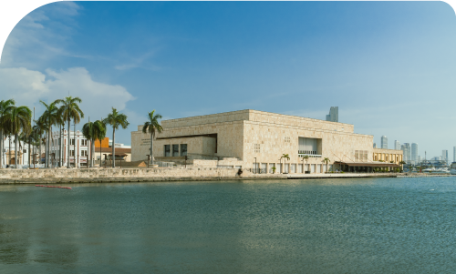 Waterfront stone cultural centre with palm trees and modern city skyline under blue sky