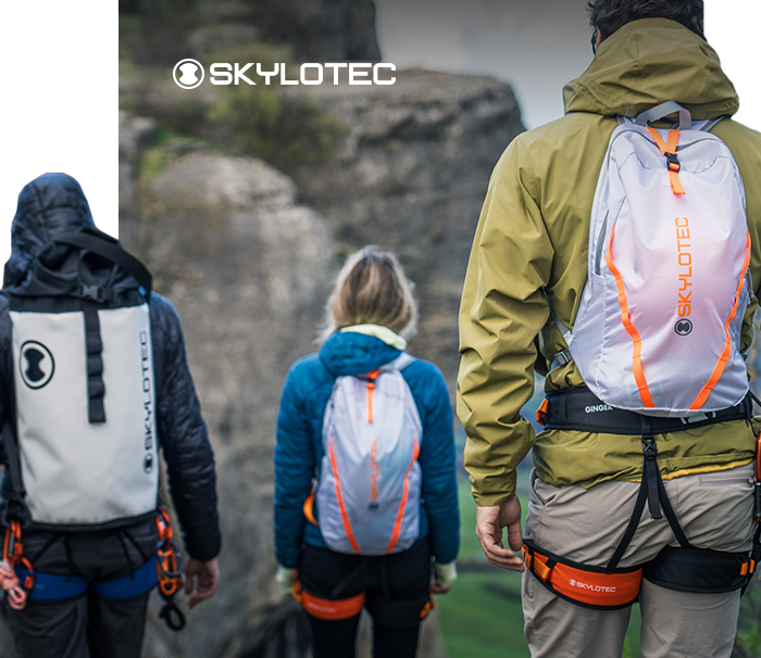 Three climbers with Skylotec backpacks and harnesses on a rocky cliff edge overlooking a valley