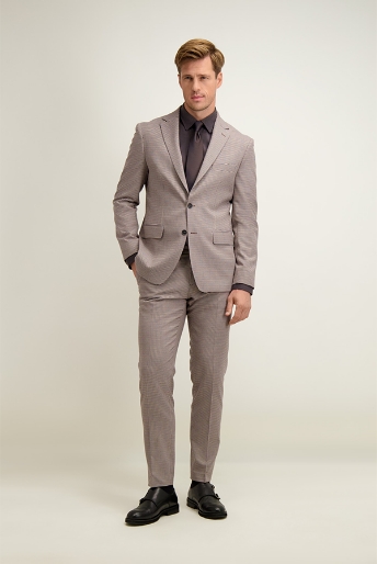 Male model in a light grey checked suit and black shirt, standing with hands in pockets against a neutral background