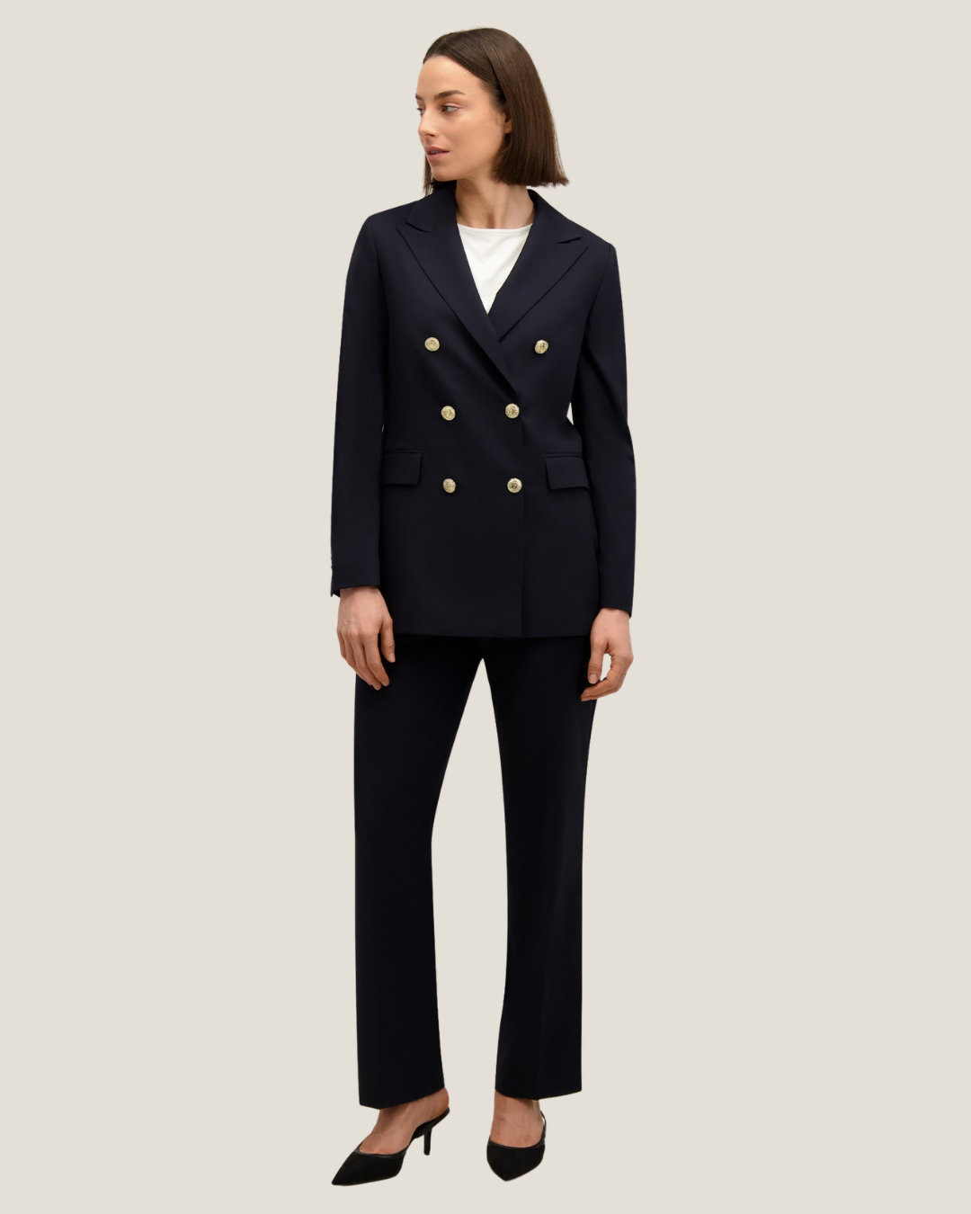 Woman modelling navy double-breasted blazer with gold buttons, matching trousers, white top and black heels