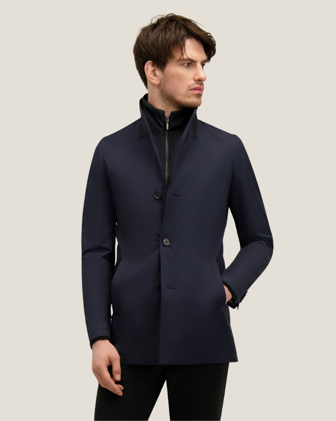 Man wearing men's navy single-breasted smart coat with zipped inner layer, hands in pockets, looking right on a pale background