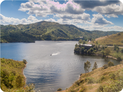 Aerial view of a lake surrounded by green hills and slopes, a small motorboat leaving a white wake under a partly cloudy sky