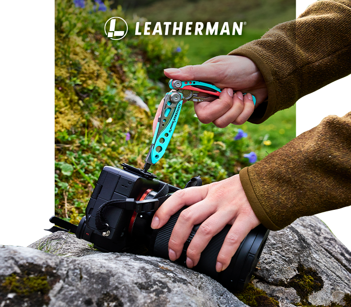 Hands using turquoise Leatherman multitool to tighten camera's mounting screw on a DSLR on a rock in grassy outdoor setting