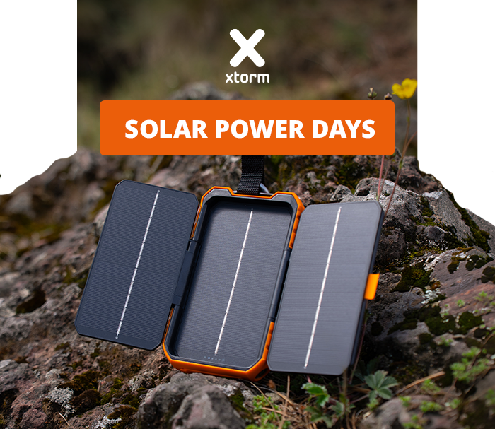 Xtorm portable foldable solar charger on rocky ground with orange trim, panels unfolded during outdoor hike